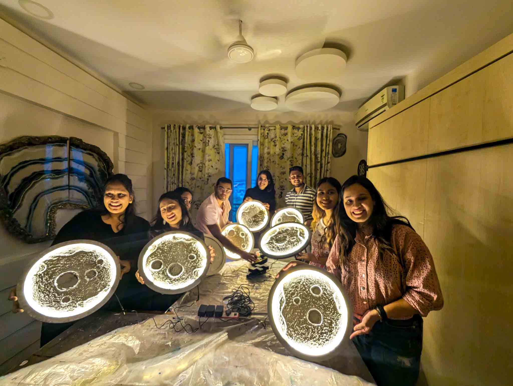 Group of participants proudly displaying their finished illuminated moon lamps in a cozy room.